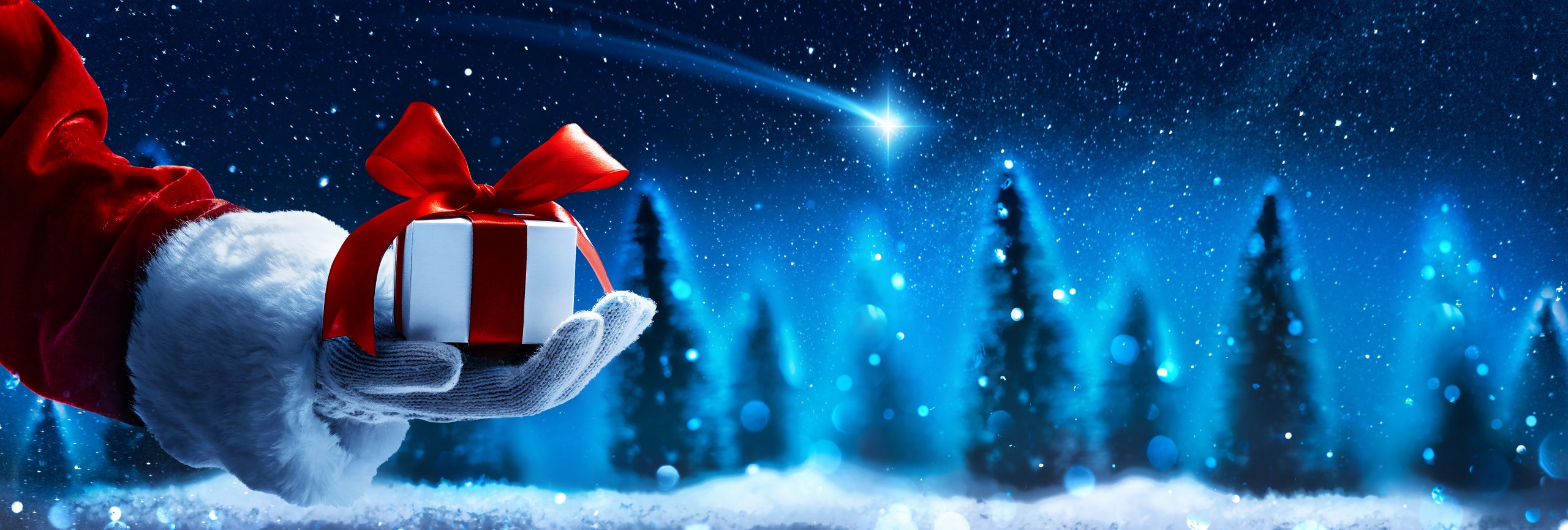 Santa hand holding Christmas gift under night sky.