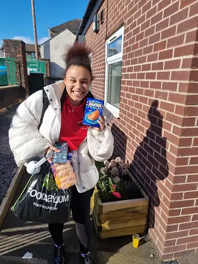Smiling person holding groceries outside brick building.