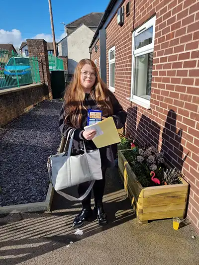 Woman with bag and letter outside brick building.