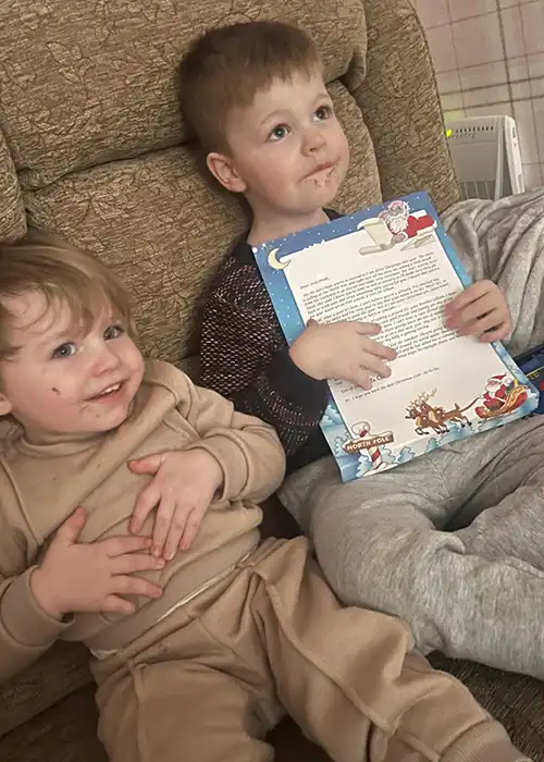 Two kids reading a colorful Santa letter on couch.