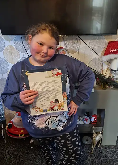 Child holding a Christmas-themed letter indoors.